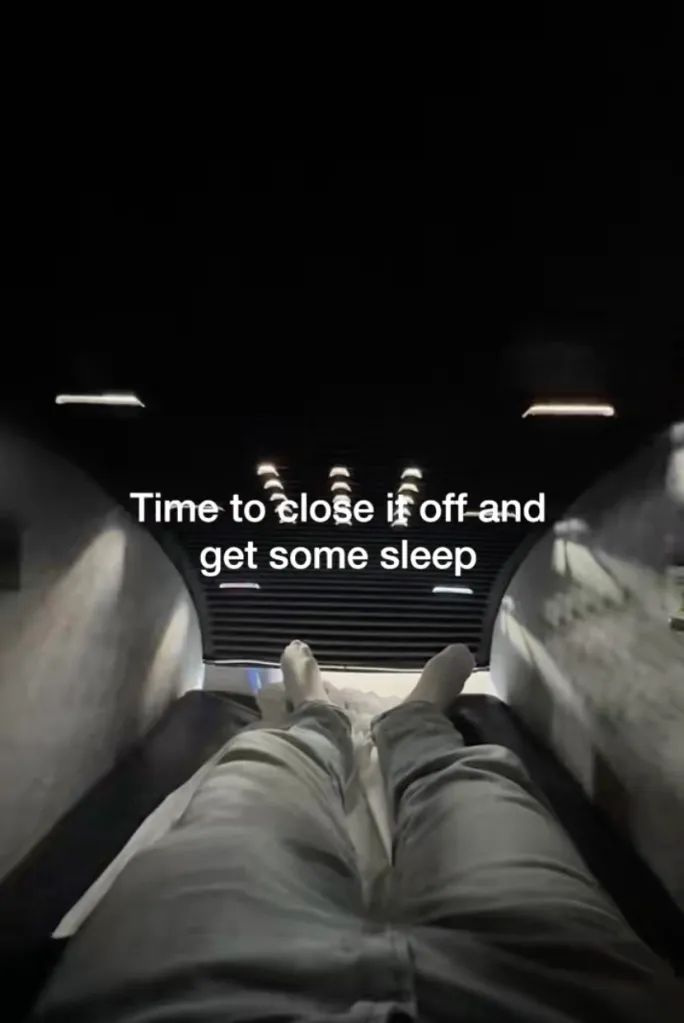 A person's legs and feet resting inside a dark sleep pod.