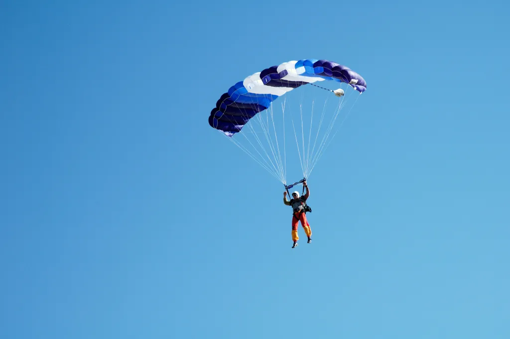 A person skydiving with a blue and white parachute against a clear blue sky.