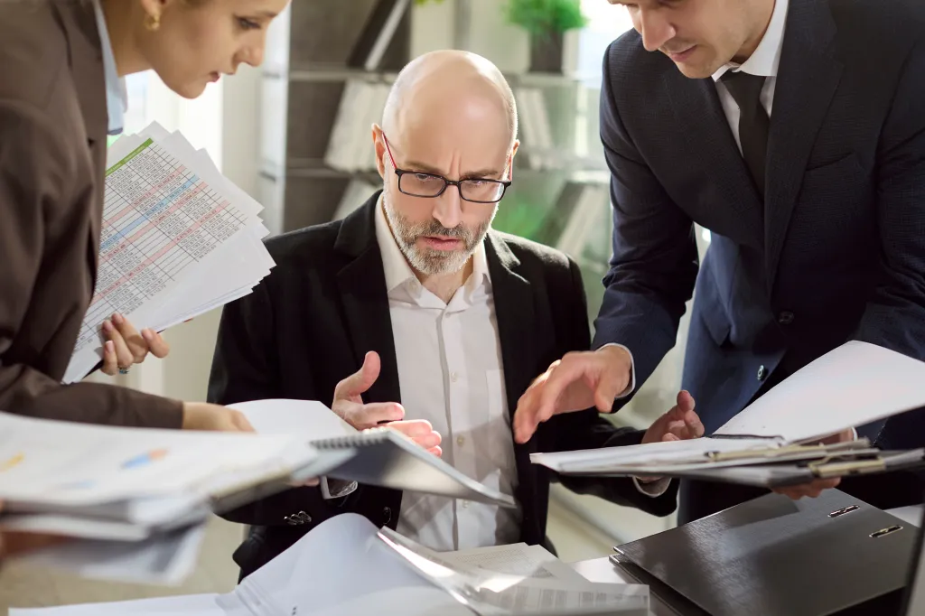 An overwhelmed manager surrounded by coworkers and paperwork.