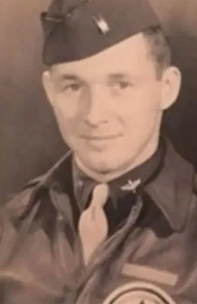 Half-body portrait of a smiling man in a military uniform with a hat, tie, and flight wings on his collar.