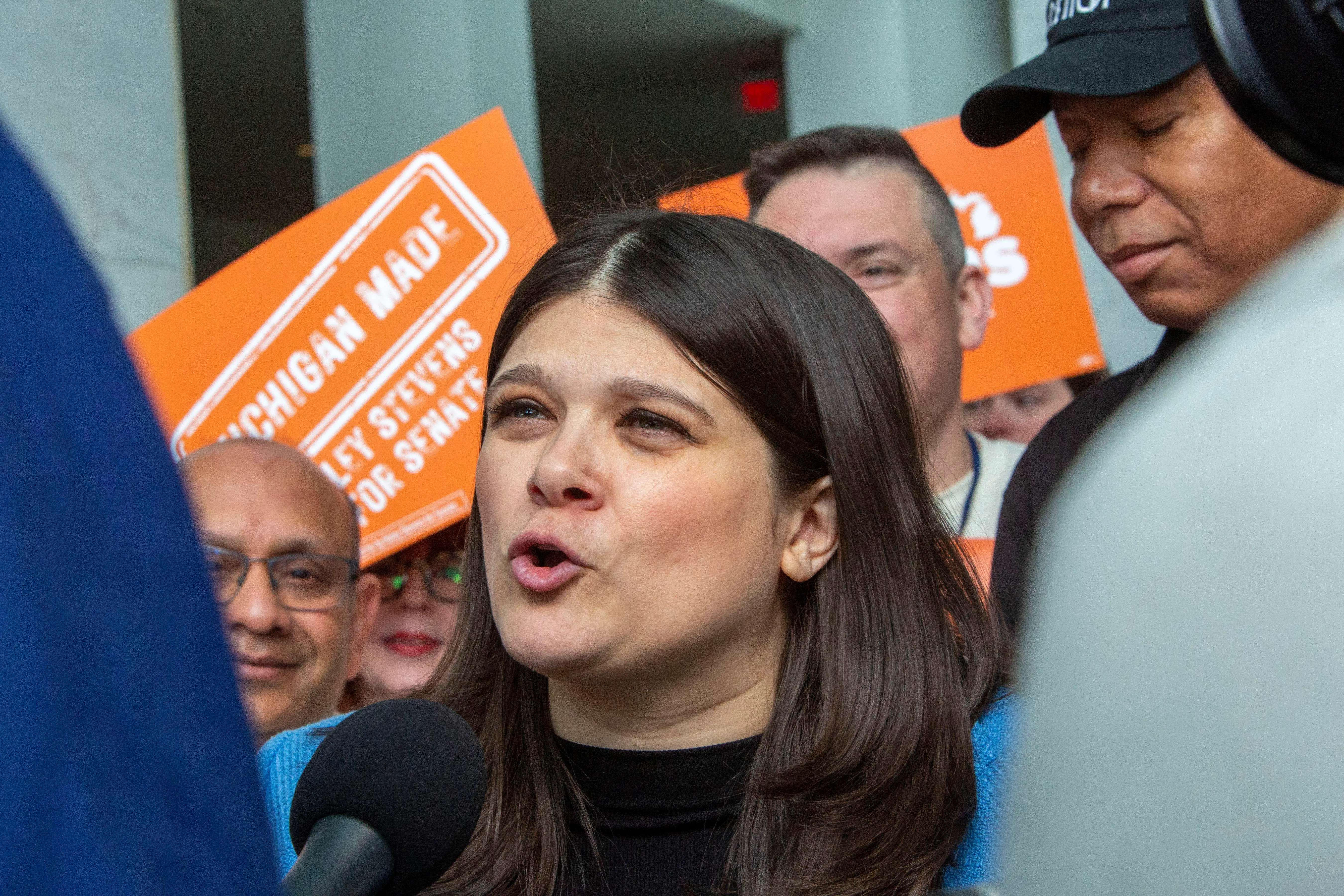 Rep. Haley Stevens speaks into a microphone, surrounded by supporters.