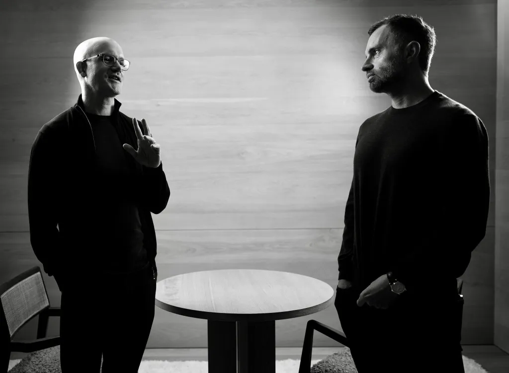Brian Armstrong (left) and David Senra (right) stand next to each other talking.