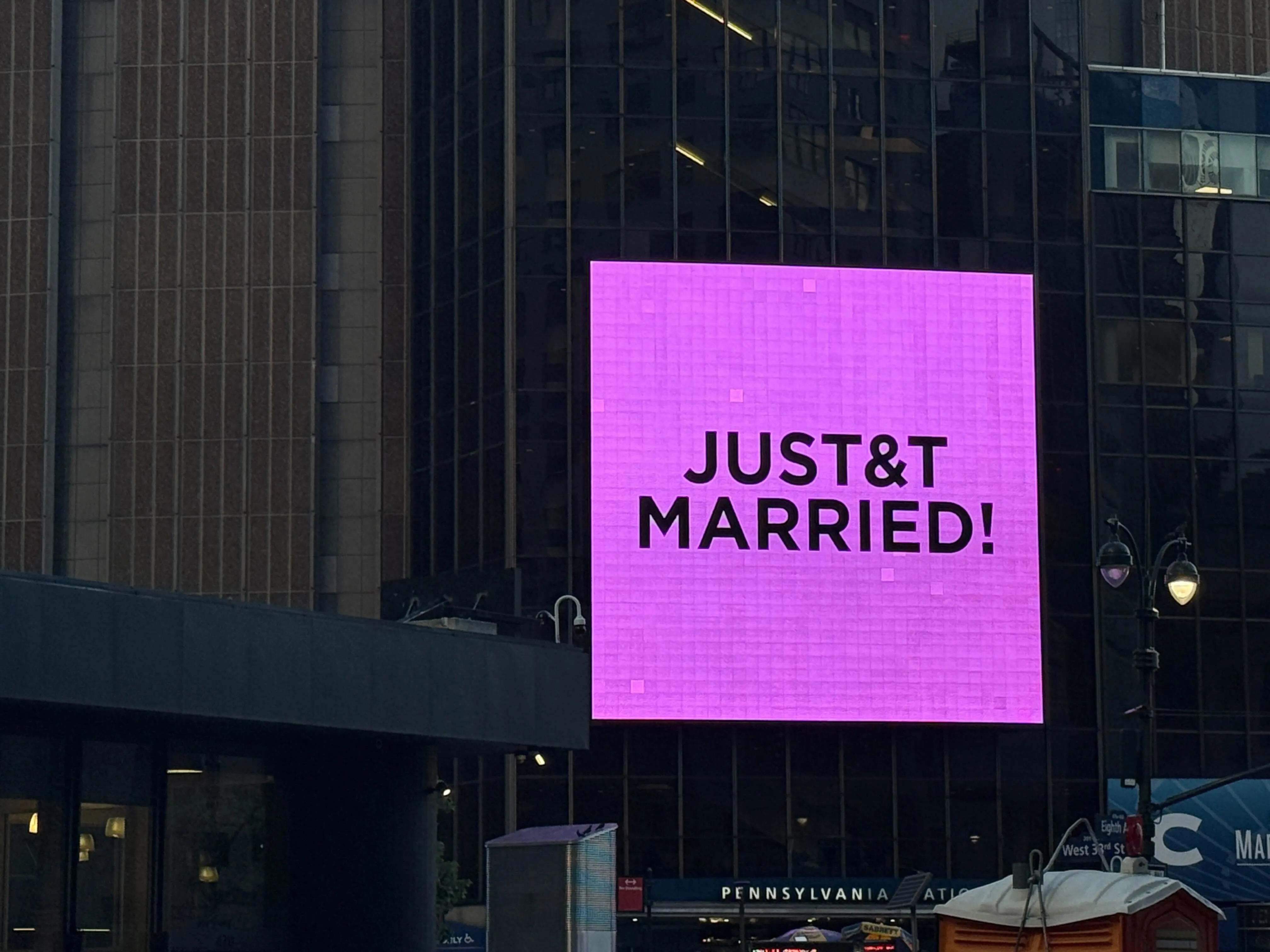 A bright pink digital billboard on a city building reads "JUST & T MARRIED!"