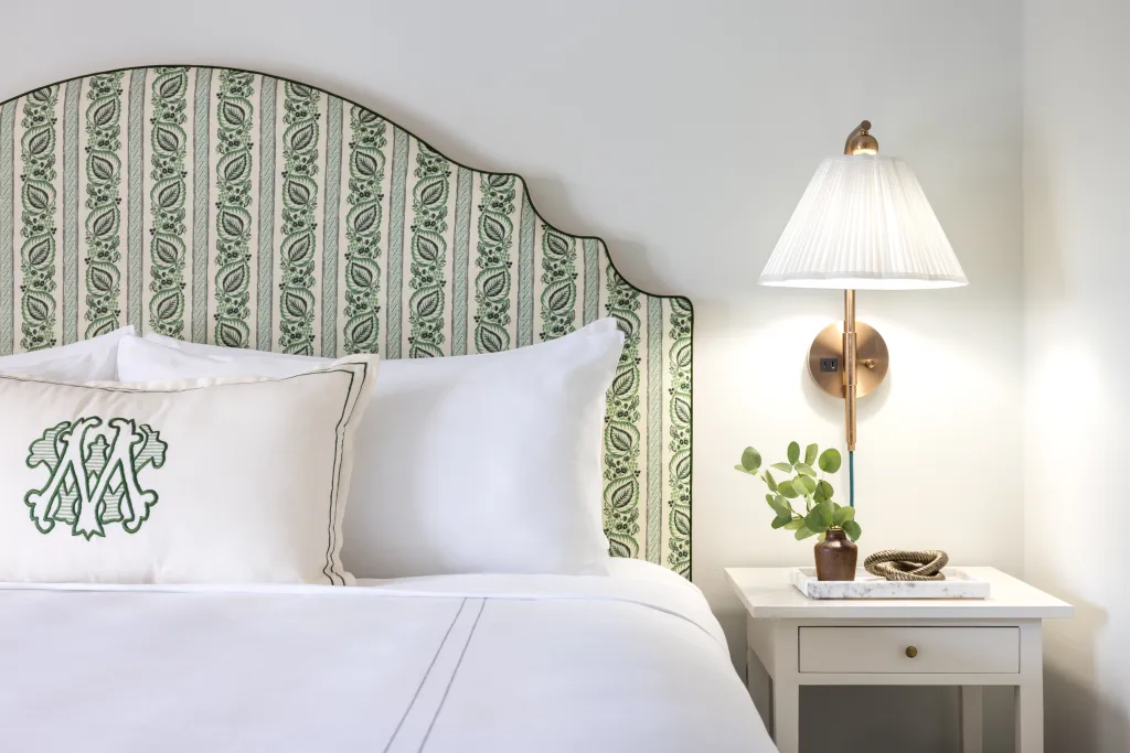 Bed with a green floral headboard and a white nightstand with a lamp.