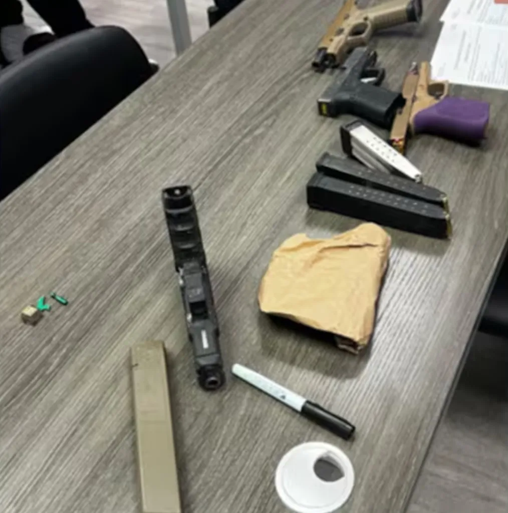 Multiple firearms, magazines, and a package on a table.