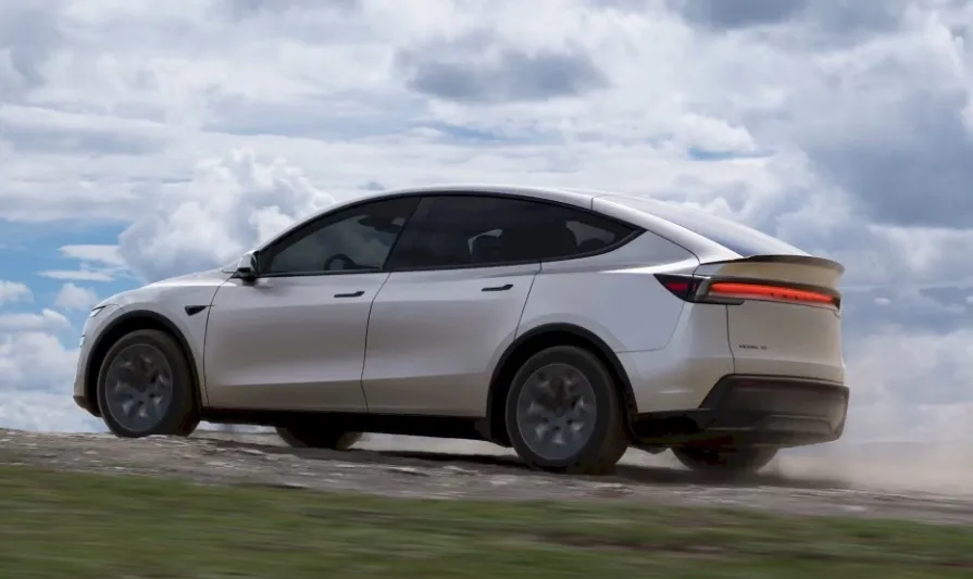 Rear view of a white Tesla Model Y driving on a dirt road, kicked up dust visible from the back tires.