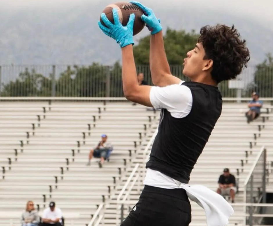 A male football player in blue gloves catching a football.