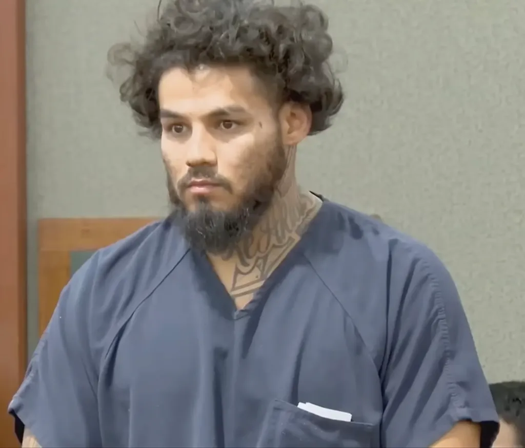 A man with curly hair, a beard, and neck tattoos wearing a blue shirt.