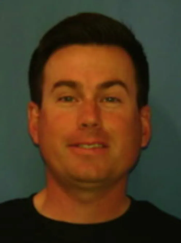 Headshot of a man with dark hair, light eyes, and a slight smile, wearing a black shirt.