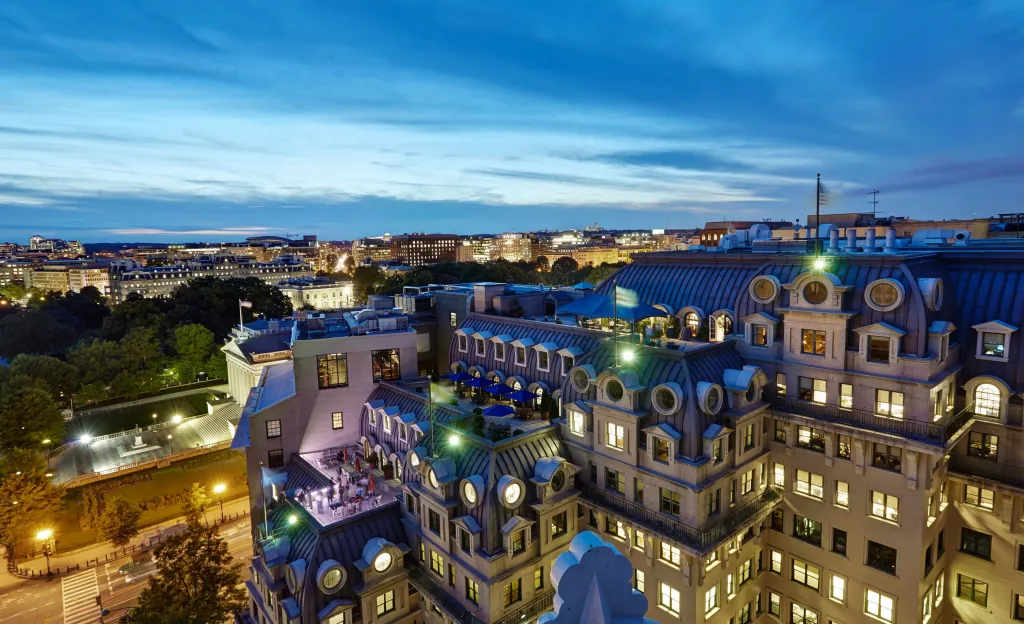 Dusk aerial view of a city with a large building and rooftop patios in the foreground.