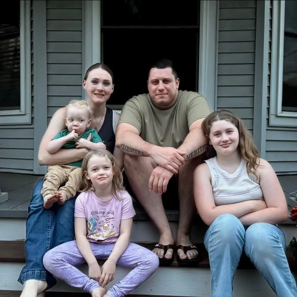 A family of five, including two adults and three children, sitting on a porch.