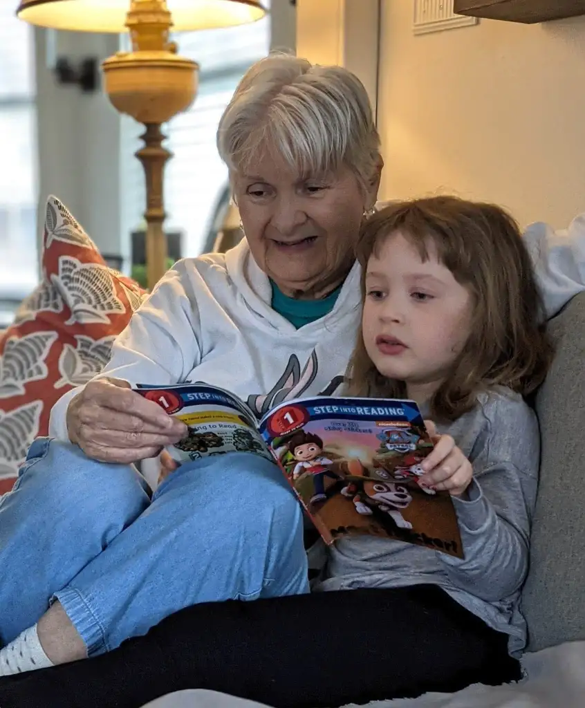 A grandmother and child reading a book together on a couch.