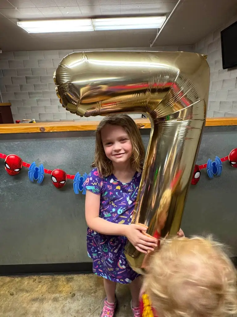 A girl holding a large golden number 7 balloon for her seventh birthday.