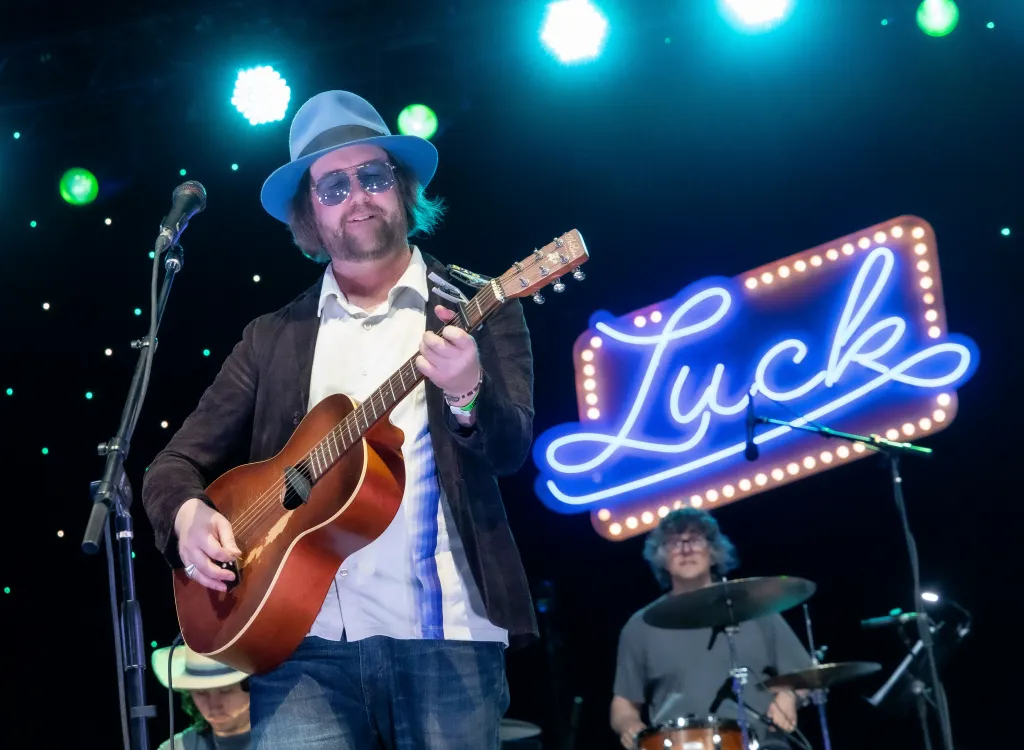Aaron Lee Tasjan performing in concert with an acoustic guitar.