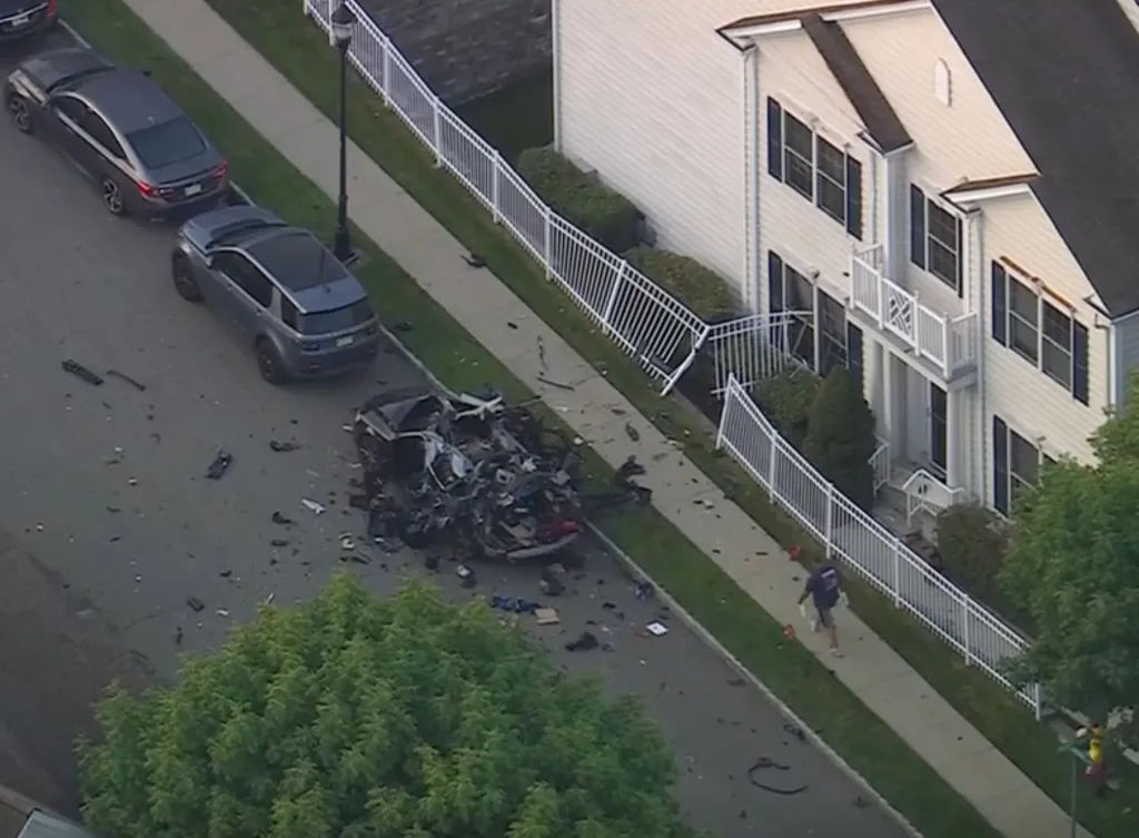 Aerial view of a street with a destroyed car, debris, and a damaged fence in front of a house.