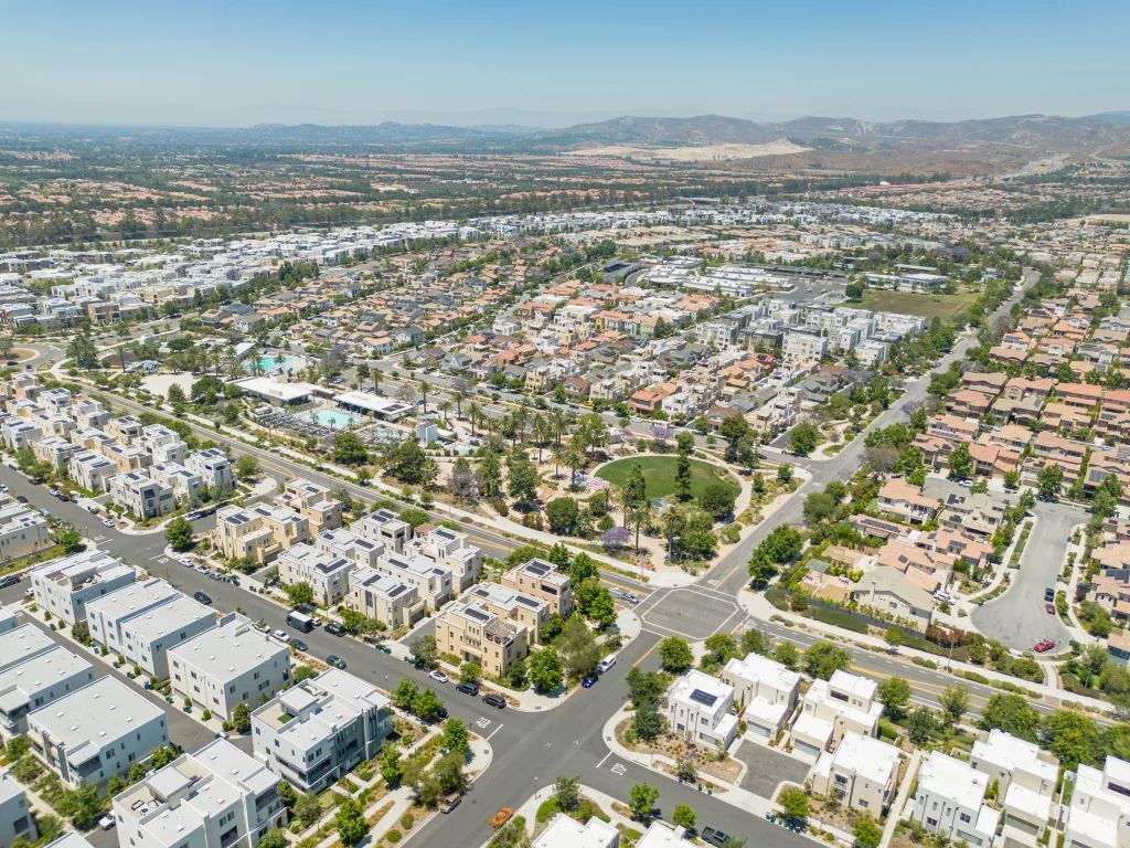 Aerial view of Irvine Great Park Village with townhouses, parks, and roads, and mountains in the distance.