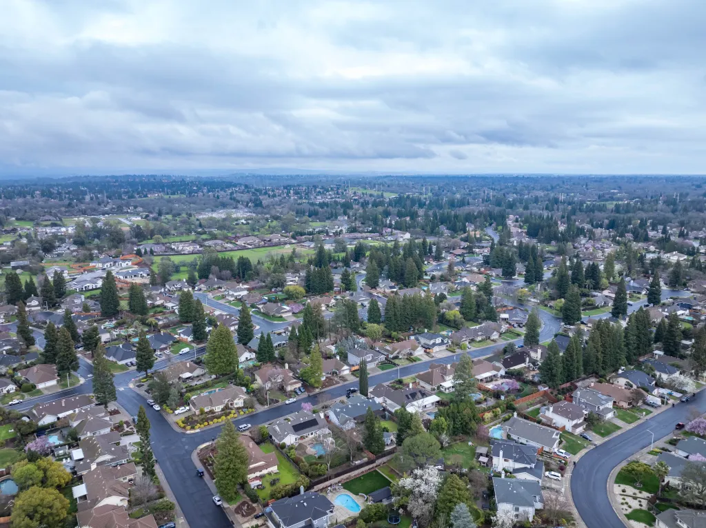 Aerial photograph of the Maidu Neighborhood in Roseville, California with green trees, streets, and homes under a cloudy sky.