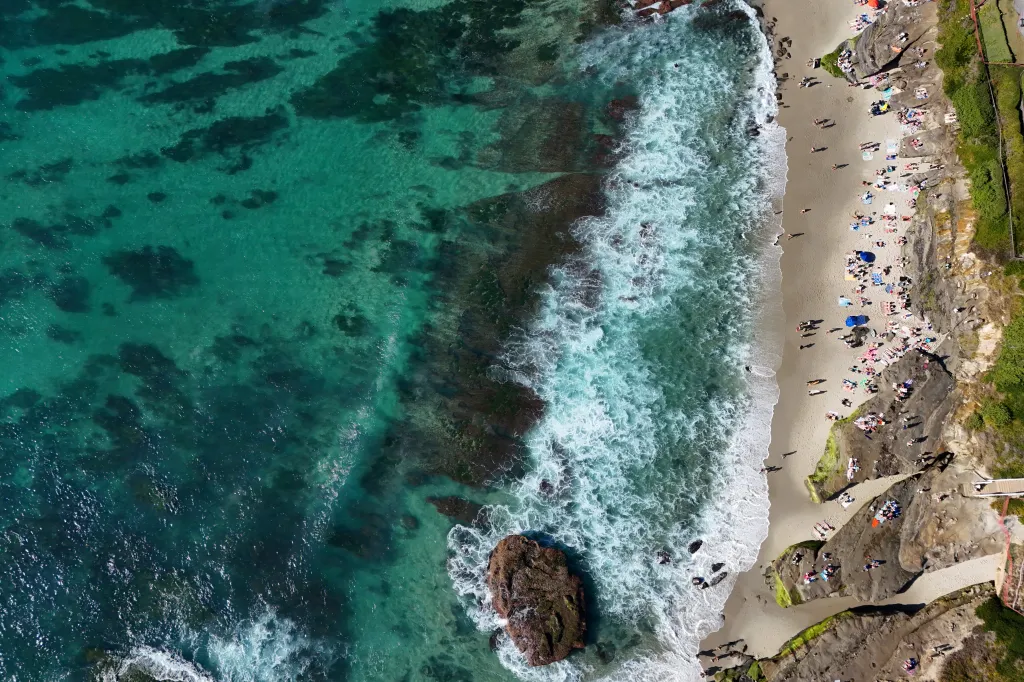 Aerial view of beachgoers at Windansea Beach in San Diego, where people are sunbathing and swimming in the clear ocean water during a winter heat wave.