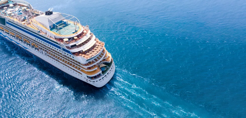 Aerial view of a white cruise ship leaving a wake in the blue ocean.