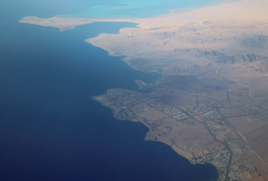 Aerial view of the Red Sea coast near Sharm el-Sheikh, Egypt, showing a city built into the desert landscape along the water.