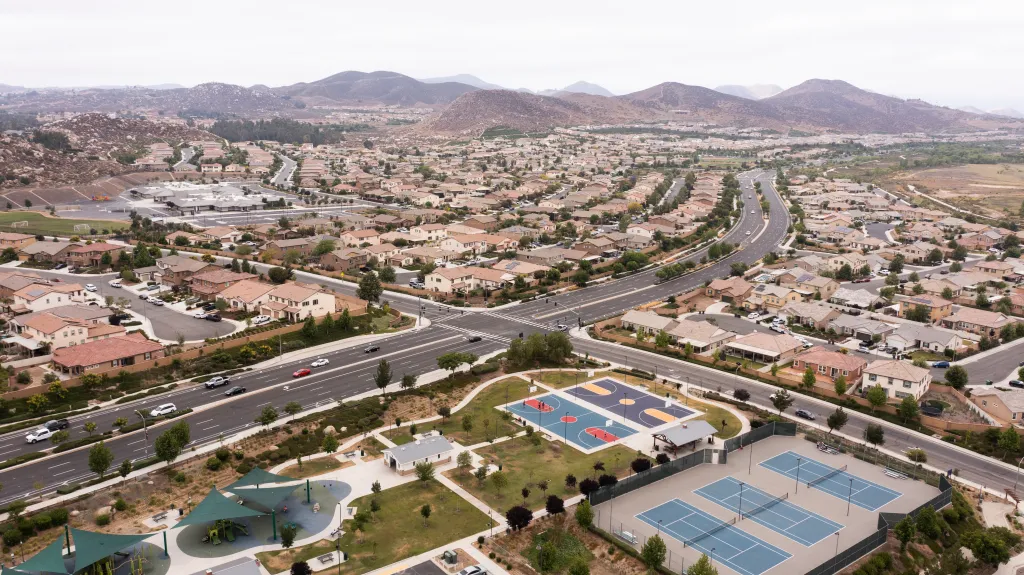 Aerial view of a sprawling residential neighborhood in Menifee, California, with houses, streets, parks, and mountains in the background.