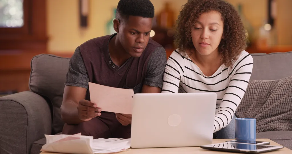 An African American couple pays bills online using a laptop.