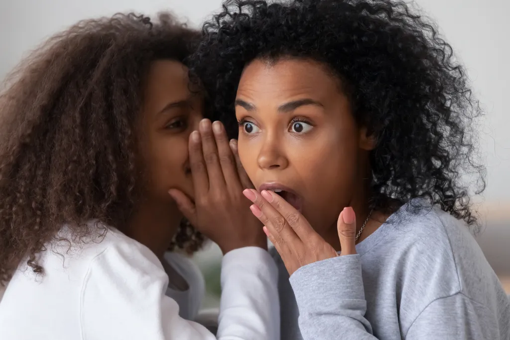 Teenage girl whispering a secret to a shocked woman.