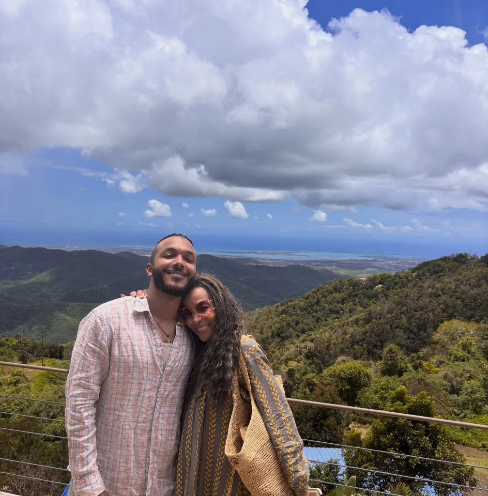 Sunny Hostin and her son Gabe Hostin smiling for a photo with mountains and ocean in the background.