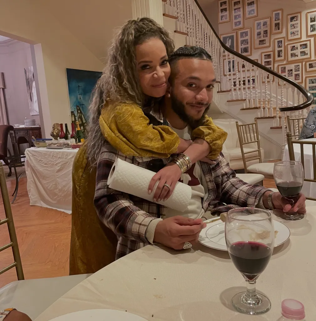 Sunny Hostin embracing her son Gabriel Hostin (aka Gabe Hostin) at a dinner table.