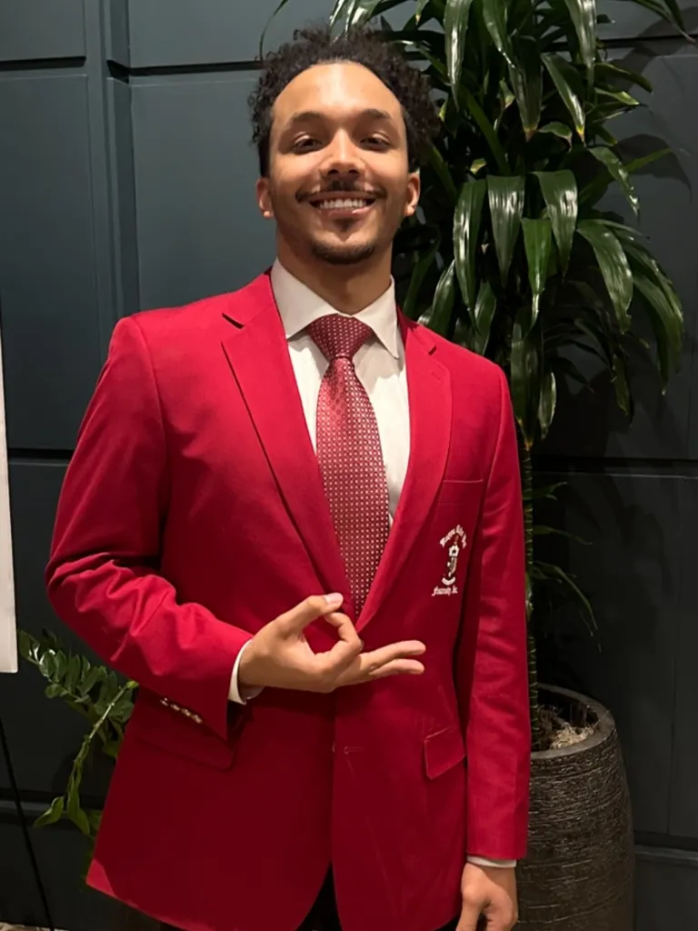 Sunny Hostin's son Gabriel Hostin (aka Gabe Hostin) in a red blazer, white shirt, and red patterned tie.