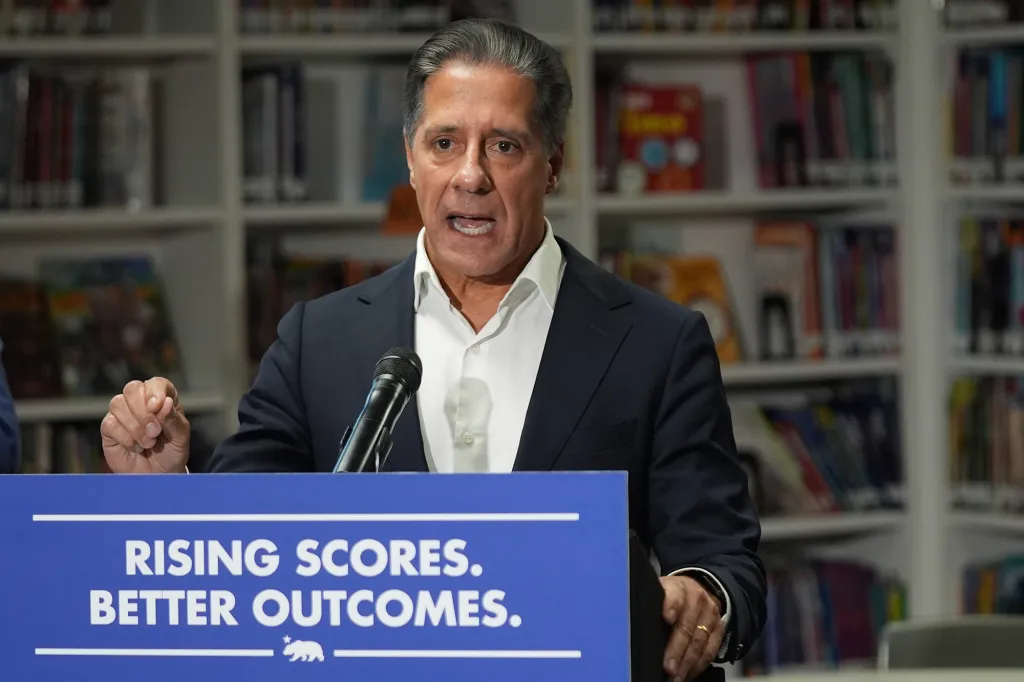 Alberto Carvalho speaks at a podium with "Rising Scores. Better Outcomes." written on it, addressing student literacy and scores.