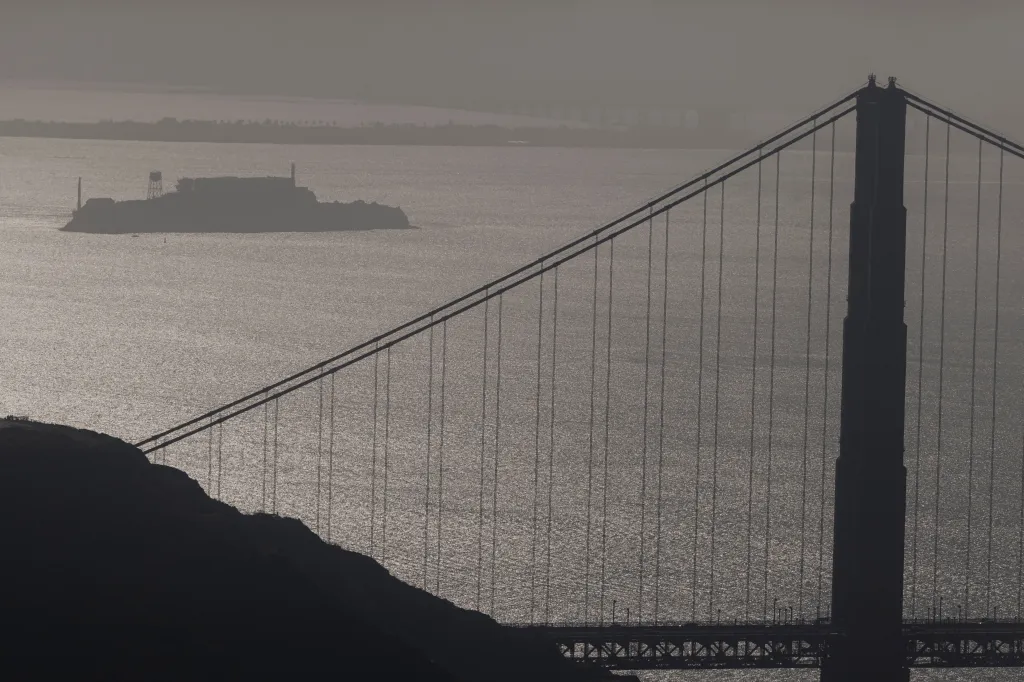 Alcatraz Island and the Golden Gate Bridge in silhouette over sparkling water.