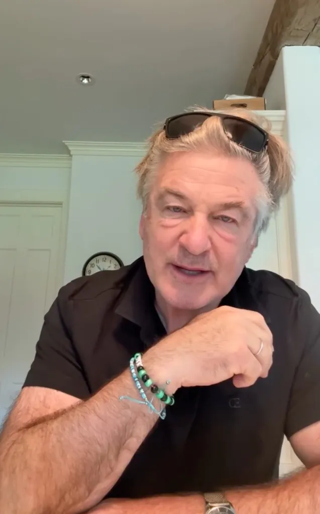 Alec Baldwin in a black shirt with sunglasses on his head and beaded bracelets on his wrist.