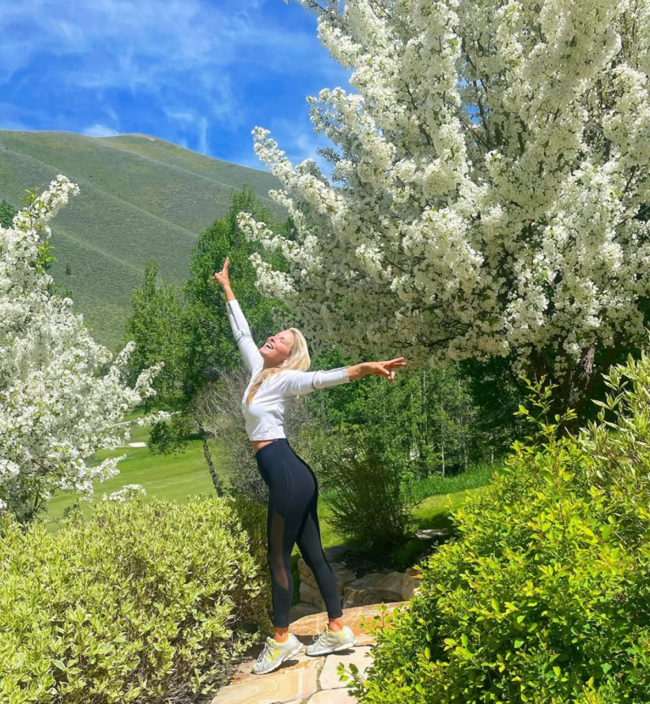Ali Larter with her arms raised, surrounded by blooming trees.