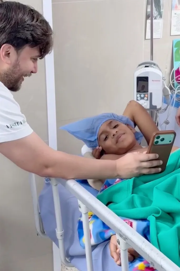 Andrés Mieles in a hospital bed, looking at a phone held by a man beside him.