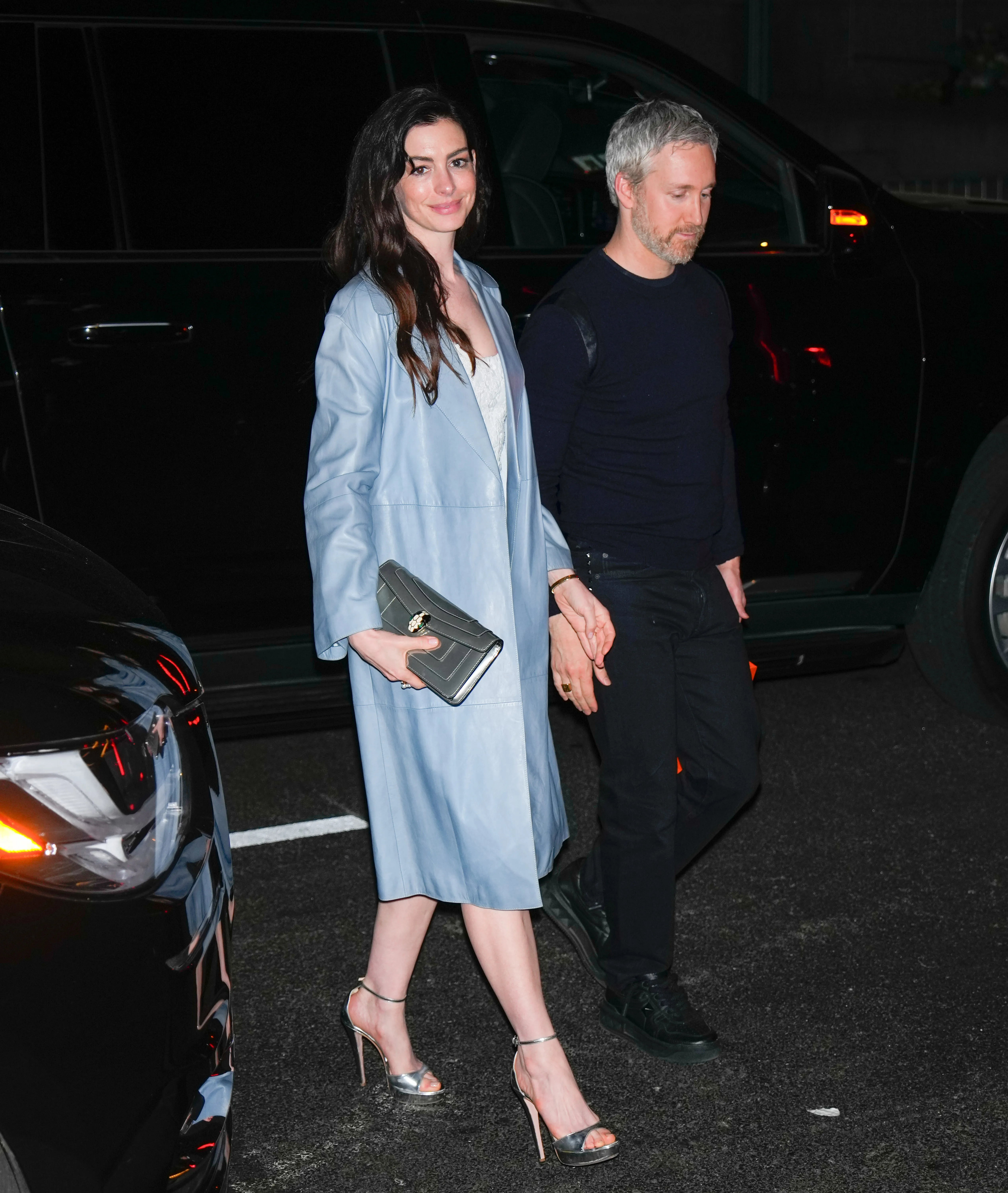 Anne Hathaway in a light blue coat and Adam Schulman holding hands while walking.