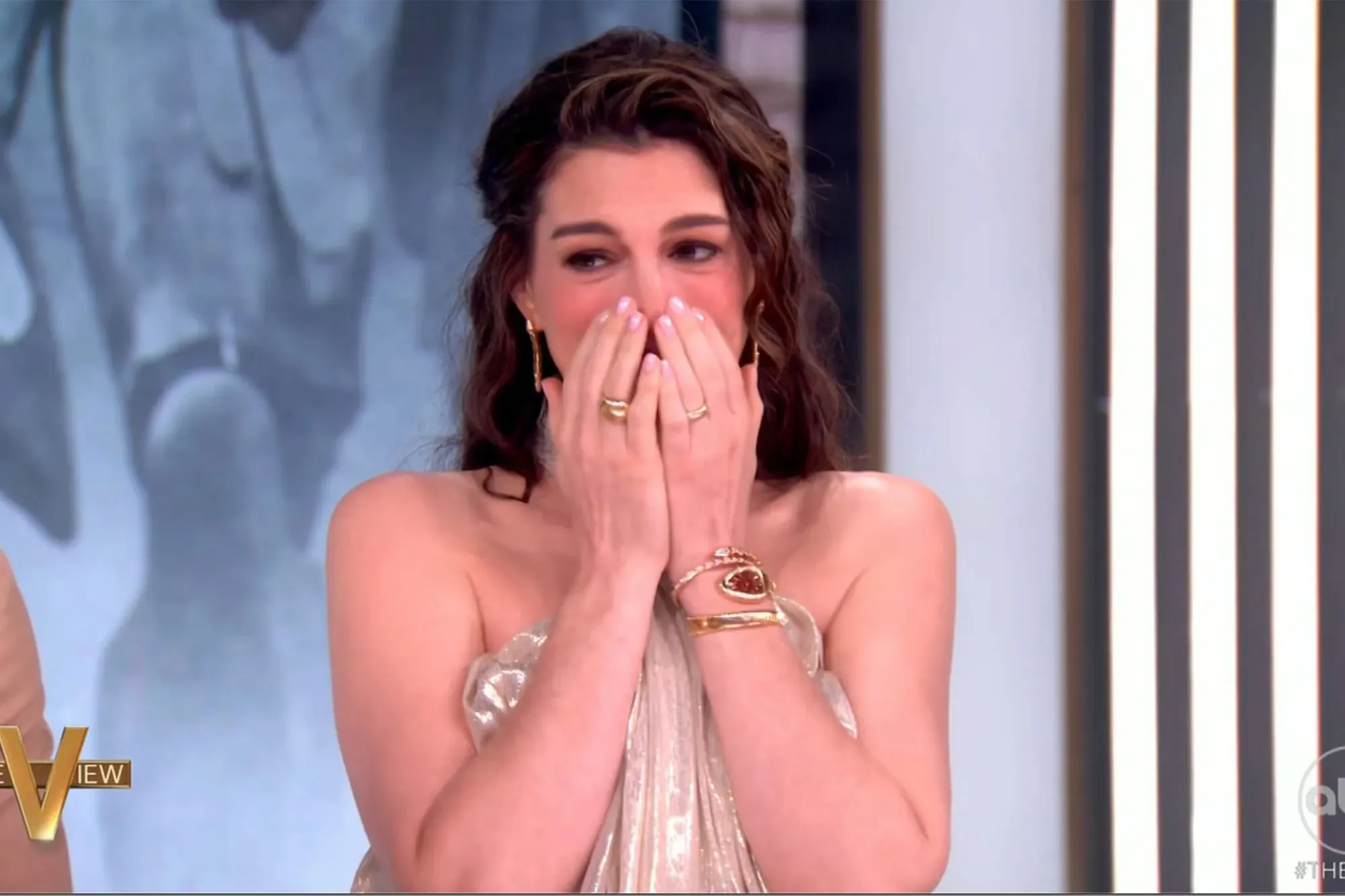 Anne Hathaway with hands over her mouth and nose.