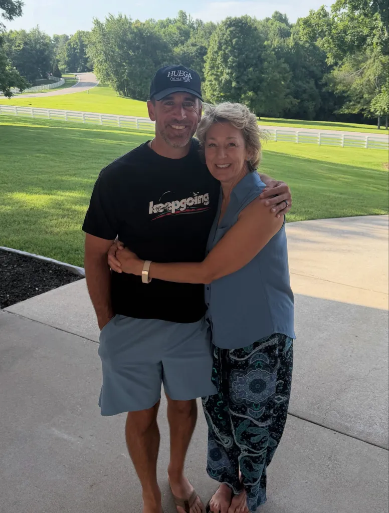 Aaron Rodgers embraces a woman in a casual outdoor setting.
