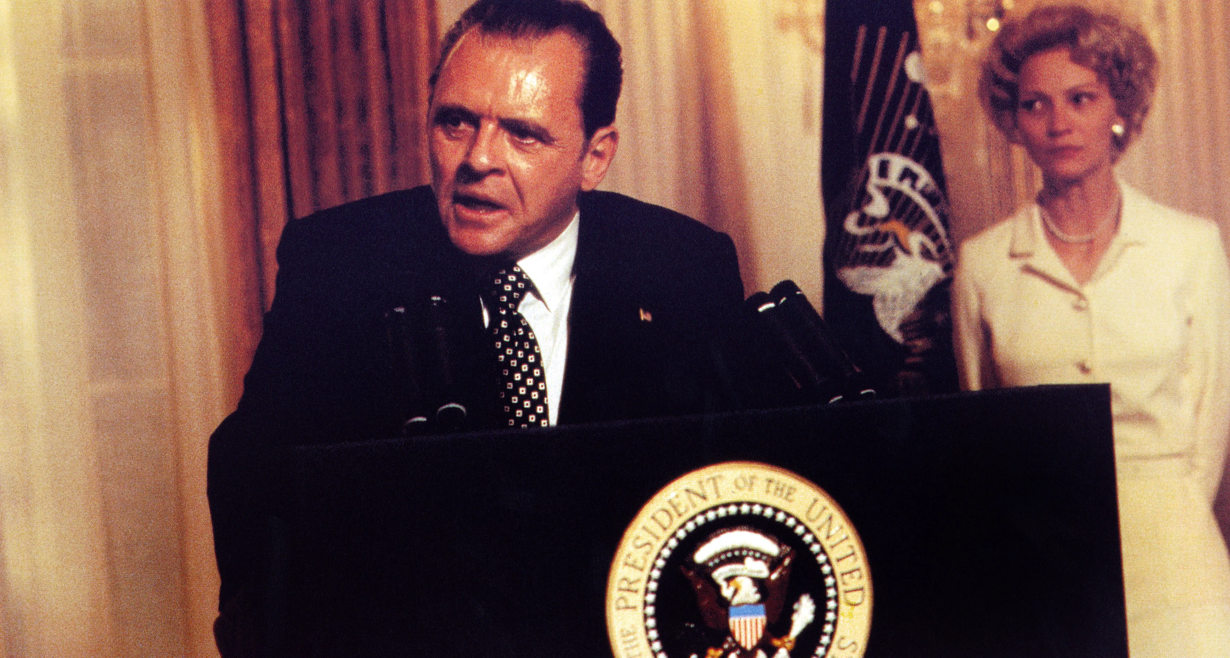 Anthony Hopkins as Richard Nixon giving a speech, with Joan Allen as Pat Nixon standing behind him, in "Nixon".