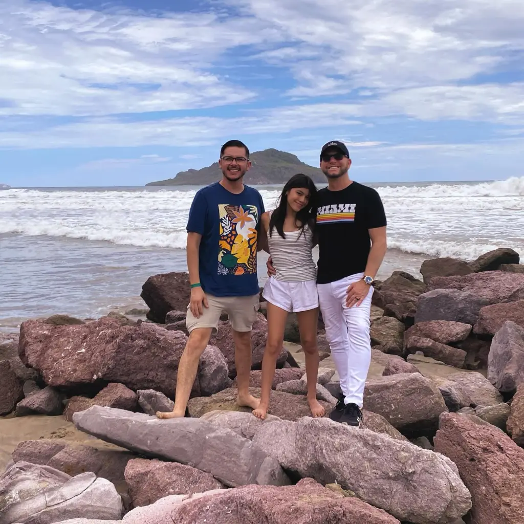 Armando Niedermeier-Rubio and two others stand on rocks at a beach.