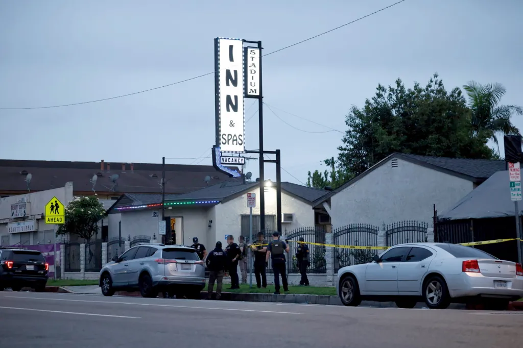 Police officers stand outside a motel with a "Stadium Inn & Spas" sign, cordoned off with yellow tape.
