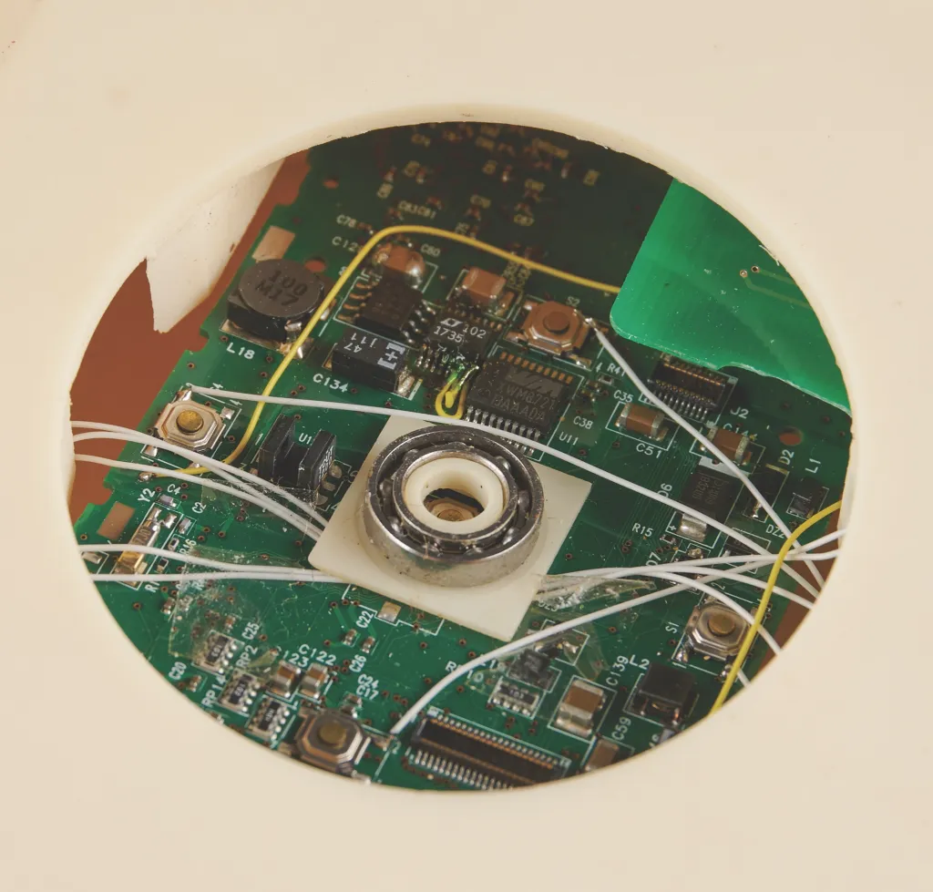 Close-up of the internal circuitry and click wheel components of a “Stealth iPod” prototype through a circular opening.