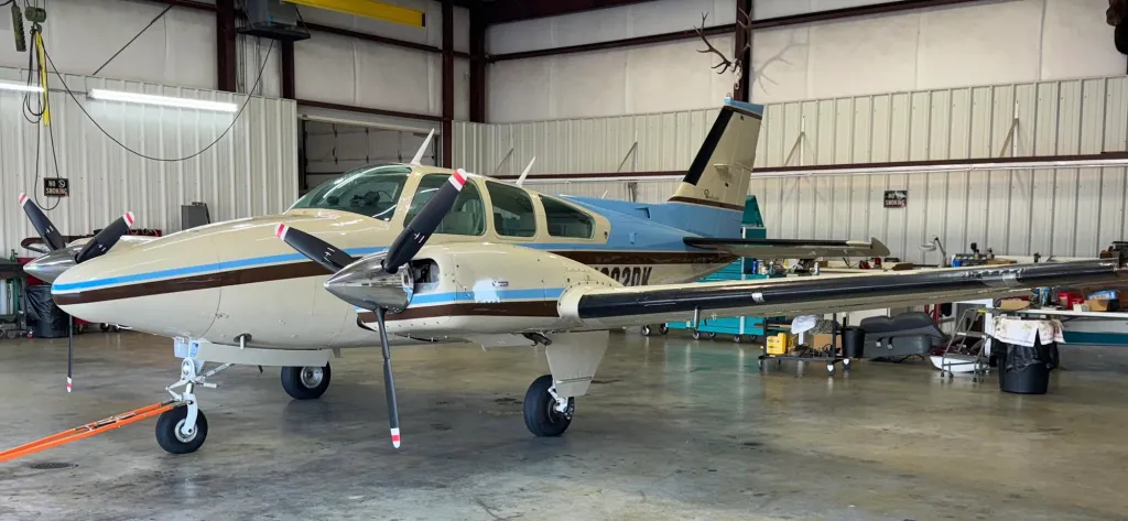 A beige, brown, and blue twin-engine Beech 95-B55 aircraft is parked in a hangar.