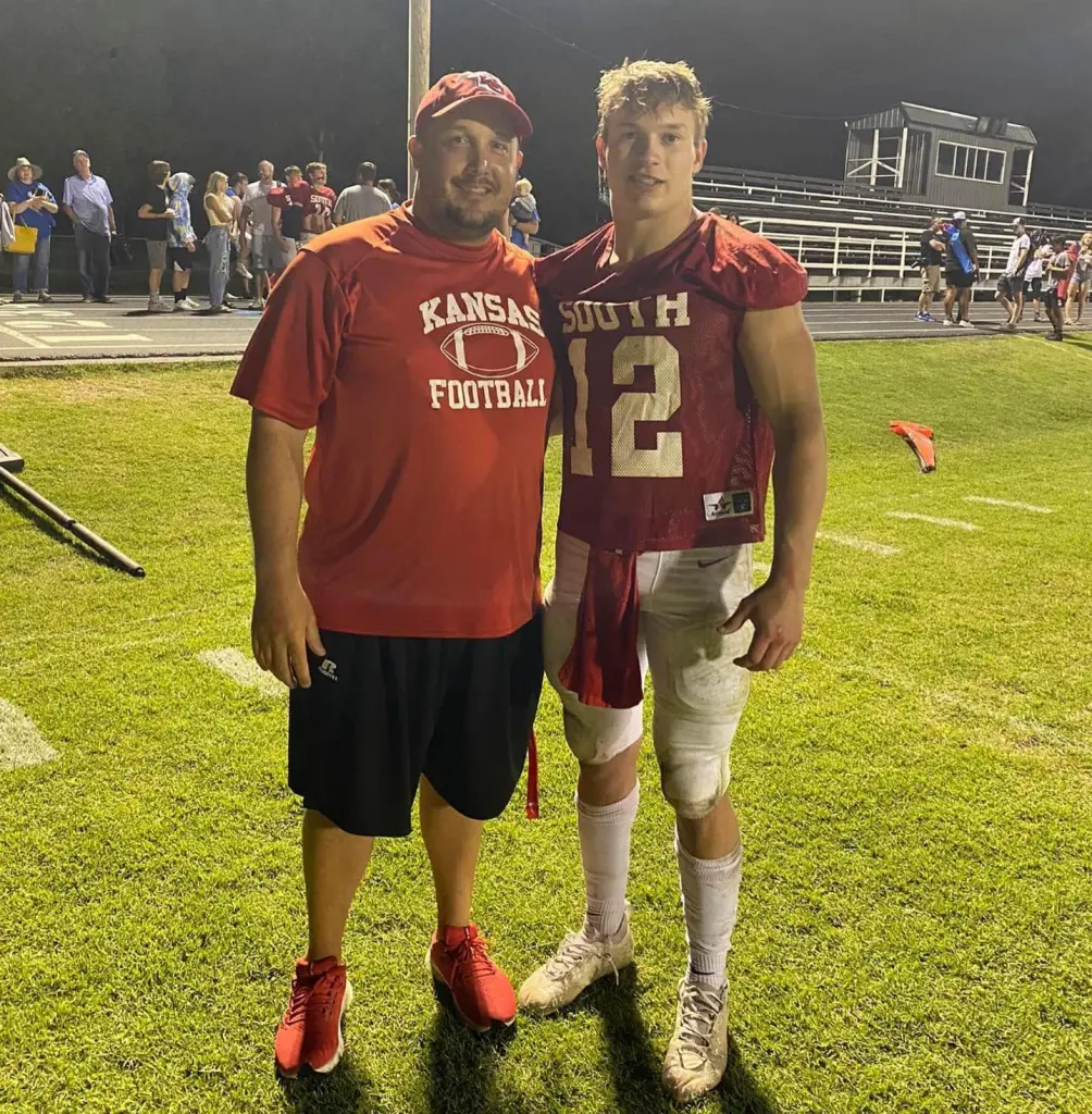 Father and son football players posing on a field at night.