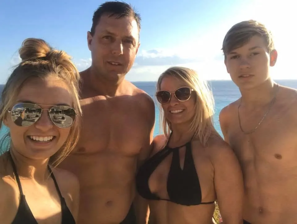 Family of four (father, mother, daughter, and son) smiling with ocean in background.