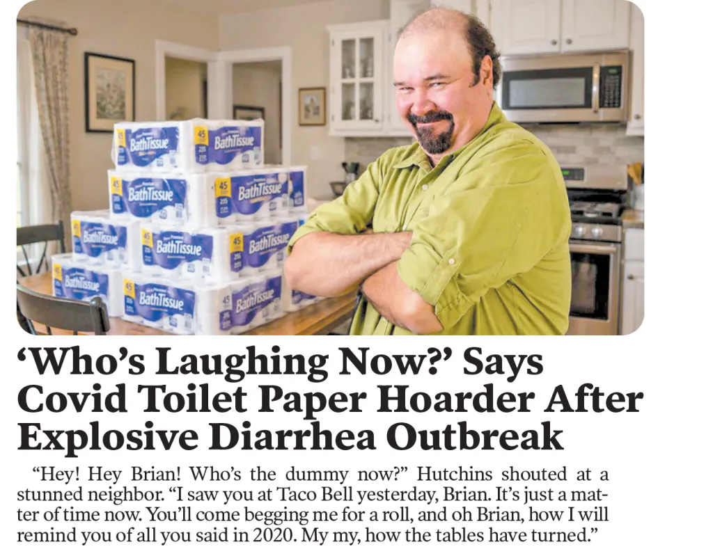 A man with folded arms smiles in a kitchen next to a large stack of BathTissue toilet paper.