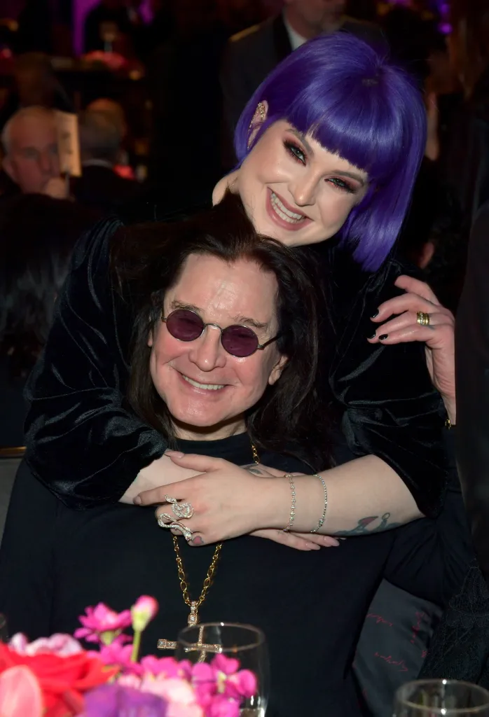Kelly Osbourne with purple hair smiling while hugging Ozzy Osbourne.