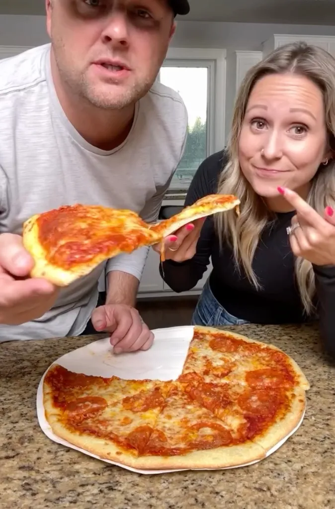 A man and woman each holding a slice of pizza from a pepperoni and cheese pizza on a paper plate.