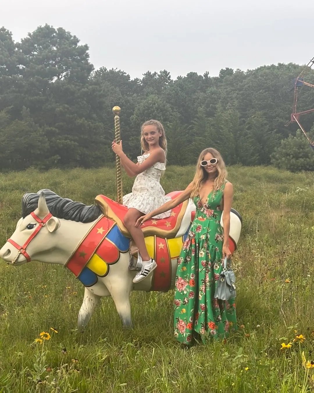 Bijou Phillips and a girl on a carousel horse in a field.