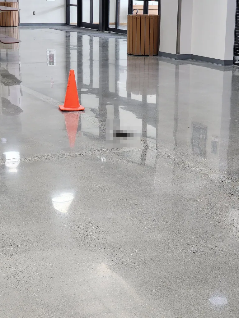 An orange cone next to black bear defecation on a shiny floor inside a mall.